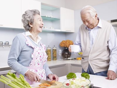 Senior asian couple talking and laughing in kitchen.